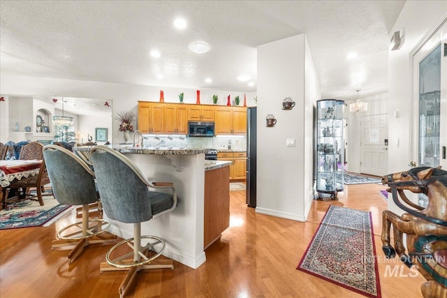 kitchen featuring light wood-style floors, a breakfast bar area, a textured ceiling, tasteful backsplash, and stainless steel appliances
