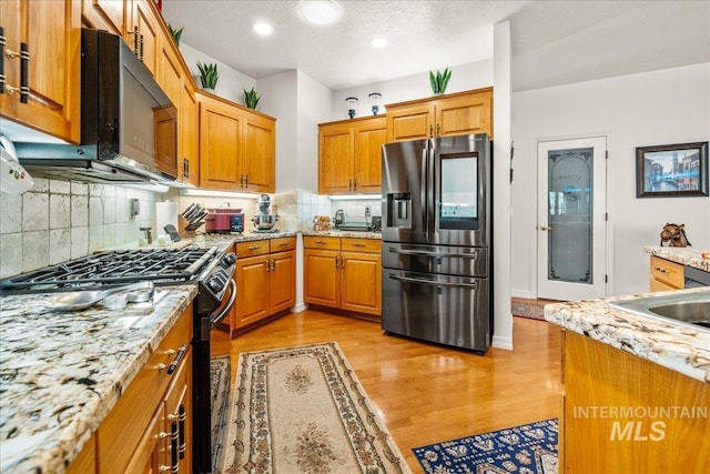 kitchen with backsplash, light stone countertops, brown cabinets, light wood-type flooring, and black appliances