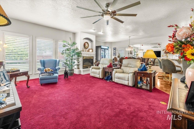 carpeted living room featuring a ceiling fan, a textured ceiling, and a glass covered fireplace