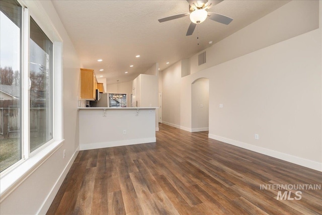 unfurnished living room with arched walkways, recessed lighting, dark wood-style flooring, visible vents, and baseboards