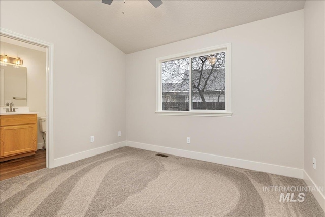 unfurnished bedroom with baseboards, connected bathroom, lofted ceiling, ceiling fan, and carpet