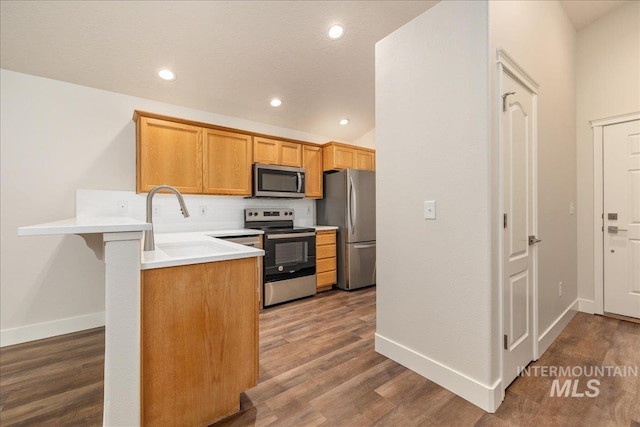 kitchen featuring stainless steel appliances, light countertops, dark wood finished floors, and a peninsula