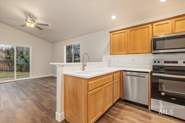 kitchen featuring lofted ceiling, stainless steel appliances, a peninsula, a sink, and light countertops