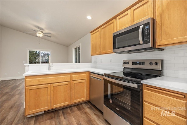 kitchen with lofted ceiling, a peninsula, a sink, light countertops, and appliances with stainless steel finishes