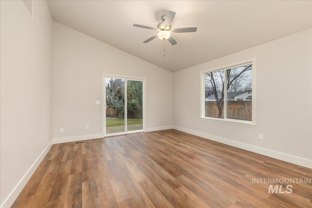 empty room with vaulted ceiling, dark wood-style flooring, a wealth of natural light, and baseboards