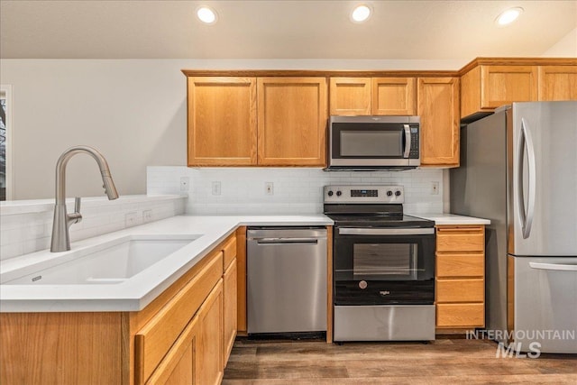 kitchen with dark wood finished floors, appliances with stainless steel finishes, a sink, light countertops, and backsplash