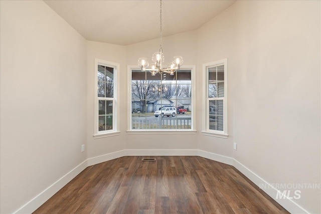 unfurnished dining area with dark wood-style floors, baseboards, visible vents, and an inviting chandelier