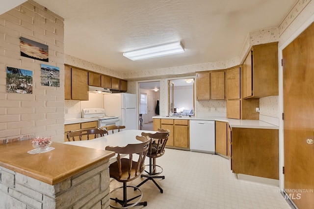 kitchen with sink, a kitchen breakfast bar, white appliances, kitchen peninsula, and a textured ceiling