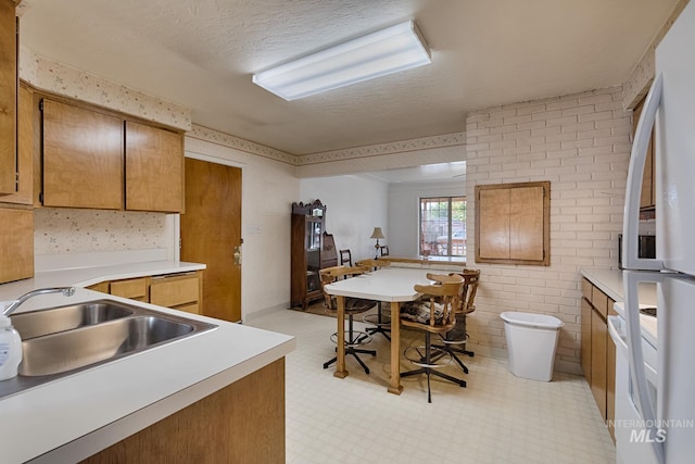 kitchen featuring sink, white refrigerator, range, kitchen peninsula, and a textured ceiling