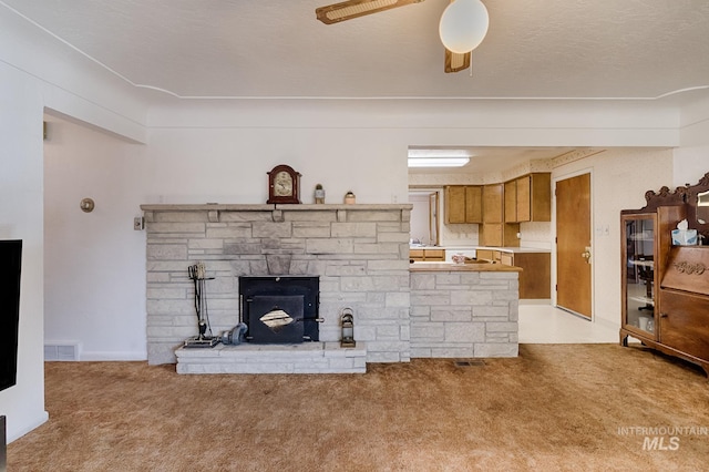 carpeted living room featuring a stone fireplace, a textured ceiling, and ceiling fan