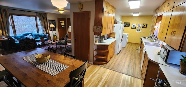 kitchen featuring washing machine and clothes dryer, sink, white fridge, and light hardwood / wood-style floors