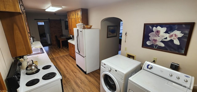 laundry room with a barn door, sink, light hardwood / wood-style floors, and washing machine and dryer