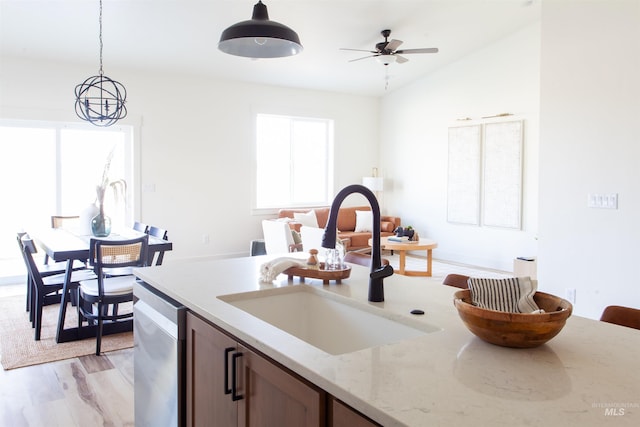 kitchen with light stone counters, a sink, decorative light fixtures, light wood-style flooring, and ceiling fan