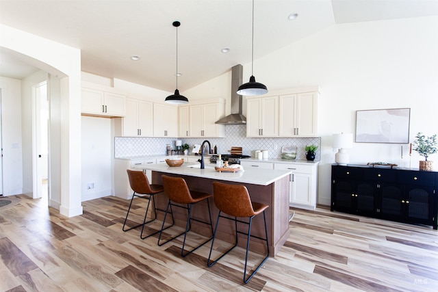 kitchen featuring wall chimney range hood, decorative backsplash, arched walkways, light countertops, and white cabinets