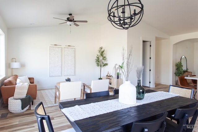 dining room featuring arched walkways, lofted ceiling, light wood-type flooring, and ceiling fan with notable chandelier