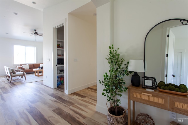 corridor featuring arched walkways, light wood-type flooring, and baseboards