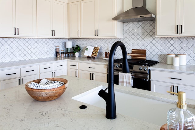 kitchen with wall chimney range hood, stainless steel gas range, light stone counters, and tasteful backsplash