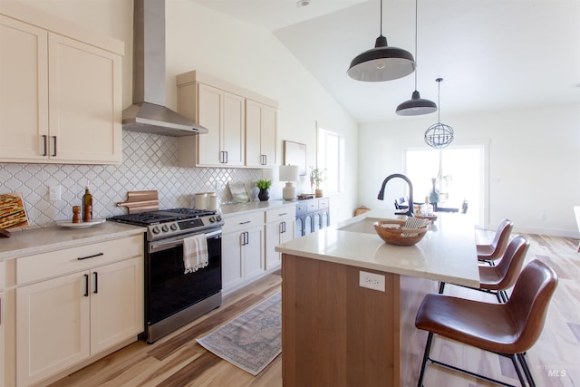 kitchen with wall chimney exhaust hood, light wood-style flooring, a sink, backsplash, and stainless steel gas range oven