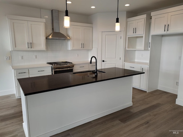 kitchen featuring wall chimney exhaust hood, stainless steel gas range, sink, decorative light fixtures, and a center island with sink