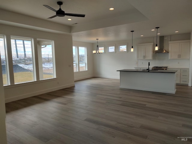 kitchen with pendant lighting, wall chimney range hood, a tray ceiling, and white cabinets