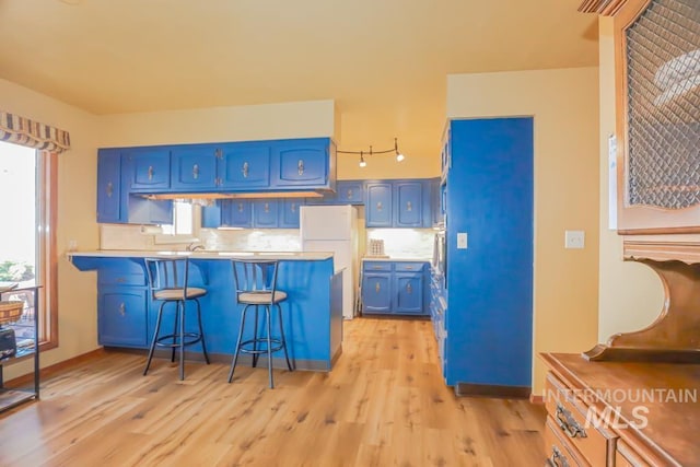 kitchen featuring a kitchen bar, light wood-type flooring, decorative backsplash, a peninsula, and blue cabinets