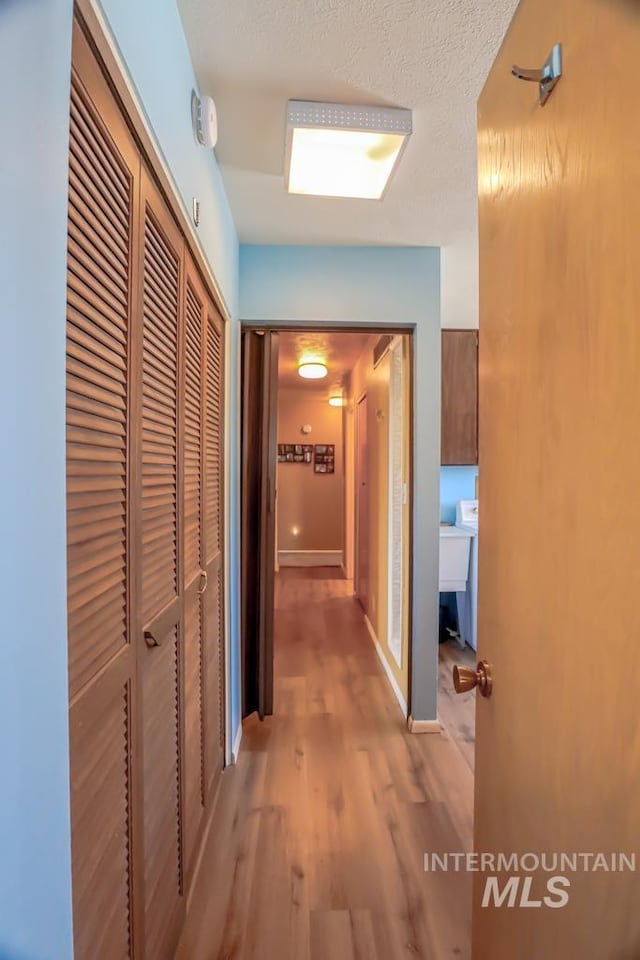 corridor featuring light wood-style floors, baseboards, and a textured ceiling