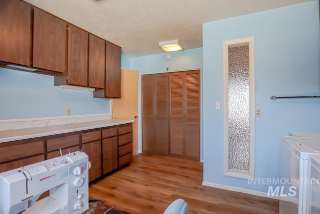 kitchen featuring light wood finished floors, light countertops, brown cabinetry, and washing machine and clothes dryer