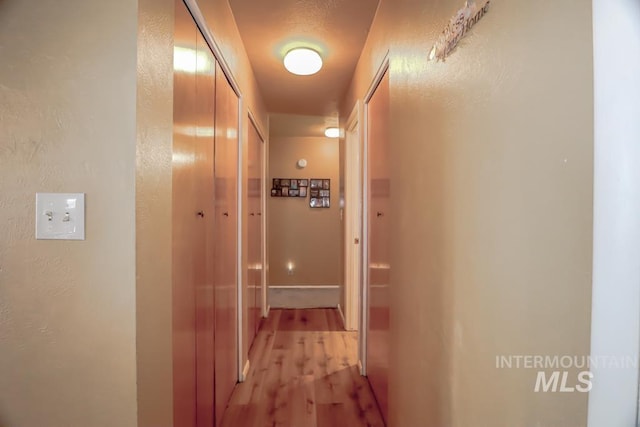 corridor with light wood-style floors and a textured wall