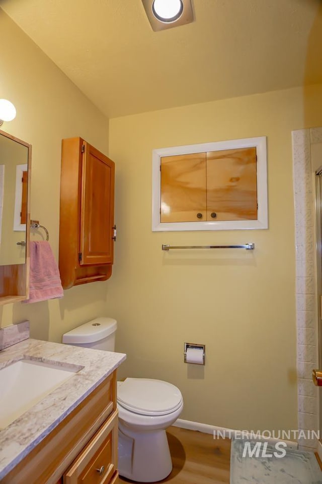 bathroom featuring baseboards, toilet, wood finished floors, vanity, and a shower