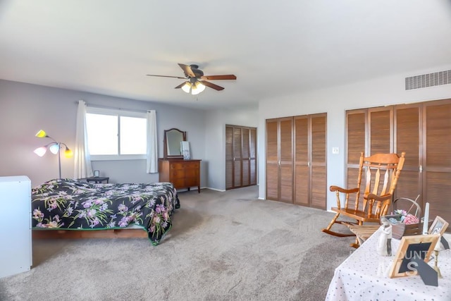 carpeted bedroom with a ceiling fan, visible vents, and multiple closets