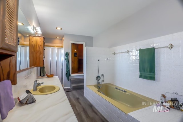 full bath with vanity, a shower, a relaxing tiled tub, and wood finished floors