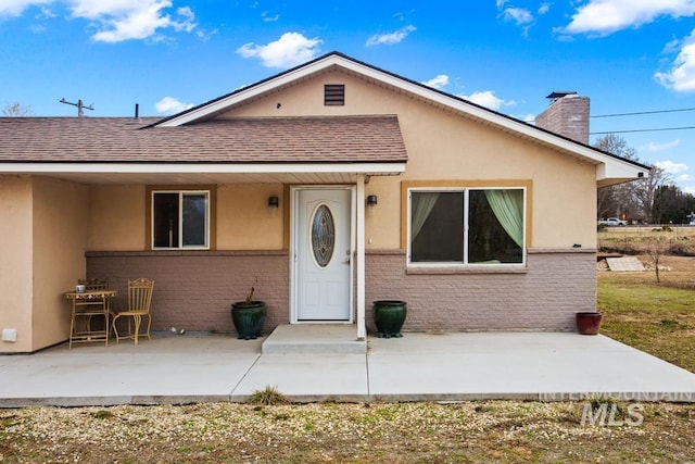 view of front of property featuring stucco siding, brick siding, a chimney, and a patio area