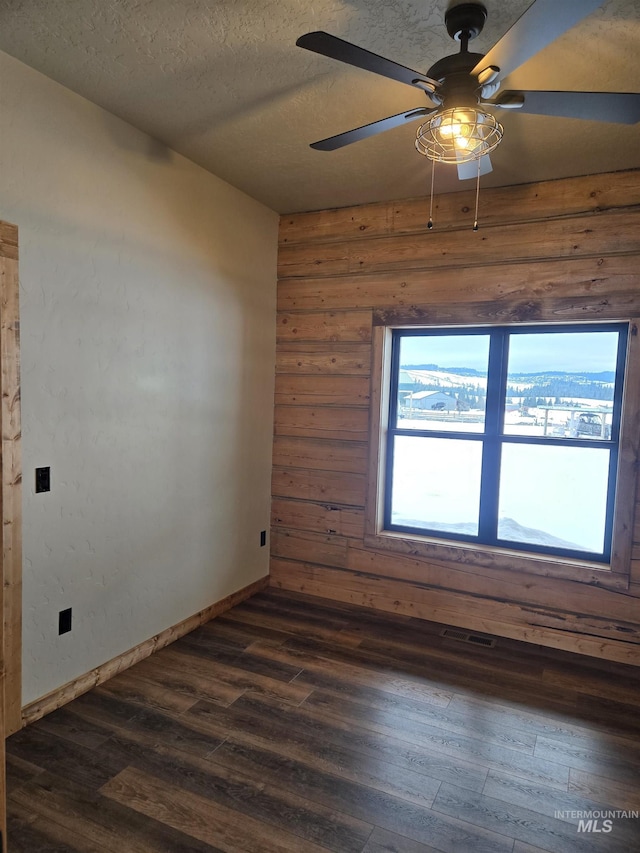 unfurnished room featuring ceiling fan, dark hardwood / wood-style floors, wooden walls, and a textured ceiling