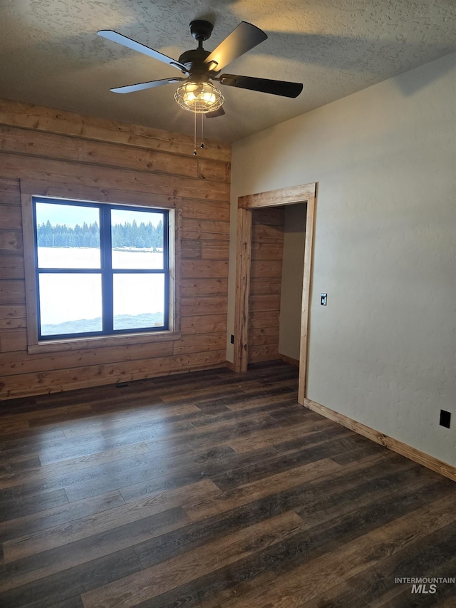 spare room featuring ceiling fan, dark hardwood / wood-style floors, wooden walls, and a textured ceiling