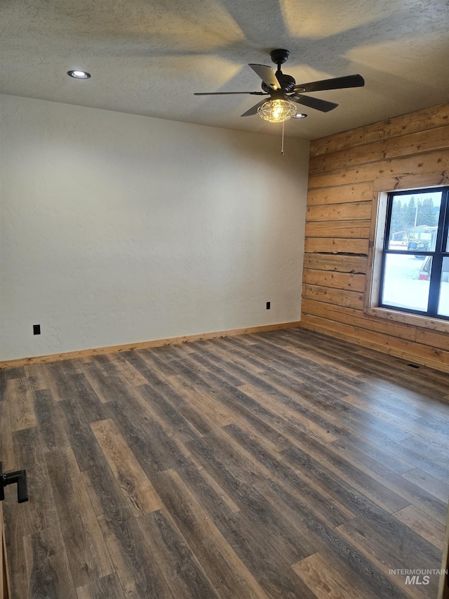 unfurnished room featuring ceiling fan, dark hardwood / wood-style flooring, wood walls, and a textured ceiling