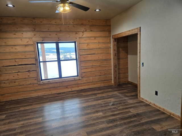 empty room with ceiling fan, dark hardwood / wood-style floors, and wood walls