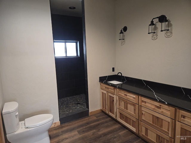 bathroom with toilet, vanity, tiled shower, and hardwood / wood-style floors