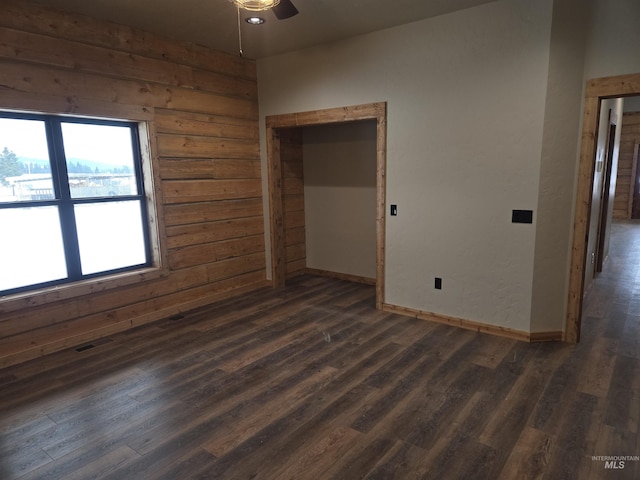 unfurnished room with dark wood-type flooring, wooden walls, and ceiling fan