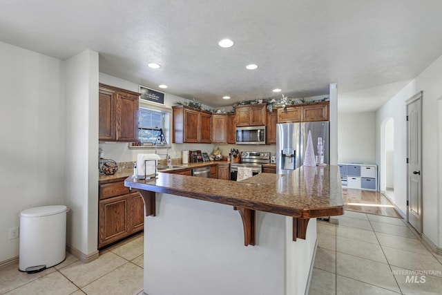 kitchen with a breakfast bar, sink, stainless steel appliances, and light tile patterned flooring