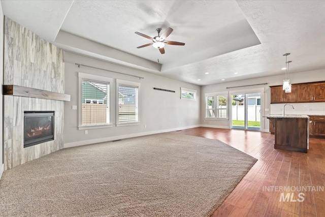 15343 Moss Creek Way, Caldwell, ID 83607 - unfurnished living room featuring a tray ceiling, a ceiling fan, a fireplace, hardwood / wood-style floors, and baseboards