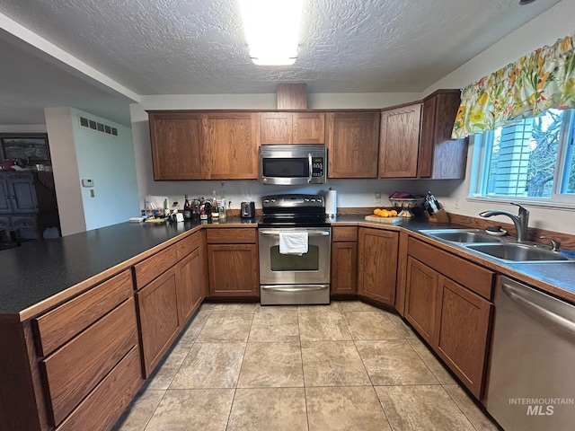 kitchen with a peninsula, visible vents, appliances with stainless steel finishes, a sink, and dark countertops