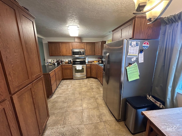 kitchen featuring brown cabinetry, a textured ceiling, appliances with stainless steel finishes, and light tile patterned floors