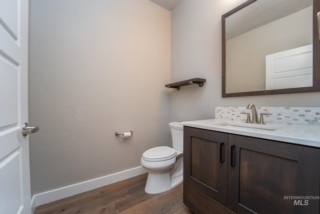 half bathroom with toilet, tasteful backsplash, wood finished floors, baseboards, and vanity