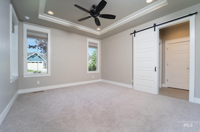 unfurnished bedroom with a barn door, a raised ceiling, light colored carpet, and multiple windows