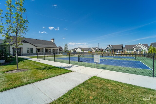 view of tennis court with a residential view, a lawn, and fence