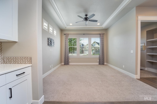 unfurnished dining area featuring a raised ceiling, recessed lighting, light colored carpet, and baseboards