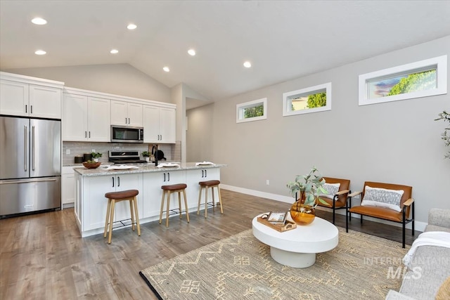 kitchen with appliances with stainless steel finishes, tasteful backsplash, an island with sink, white cabinets, and a kitchen bar