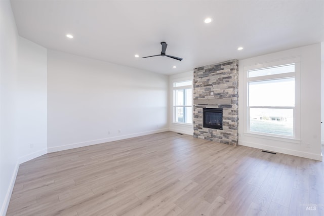 unfurnished living room with ceiling fan, light wood-type flooring, and a stone fireplace