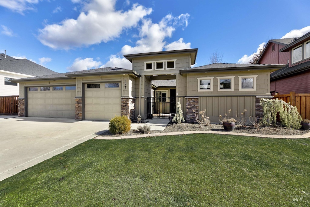 prairie-style home with stone siding, fence, an attached garage, concrete driveway, and a front lawn