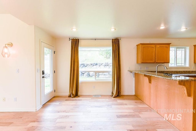 1962 E 6th St, Moscow, ID 83843 - kitchen featuring light wood-style flooring, a kitchen bar, brown cabinetry, stone counters, and visible vents